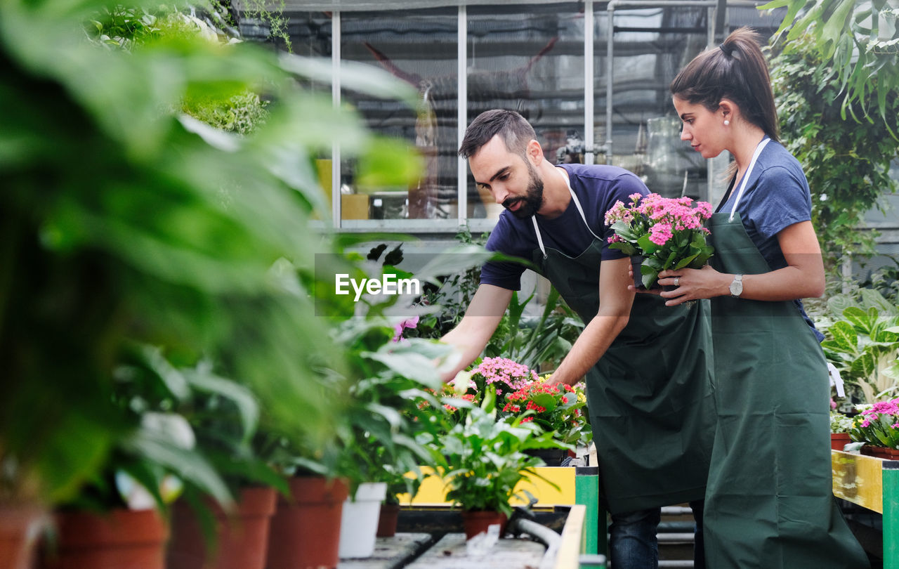 MAN AND WOMAN STANDING BY POTTED PLANT