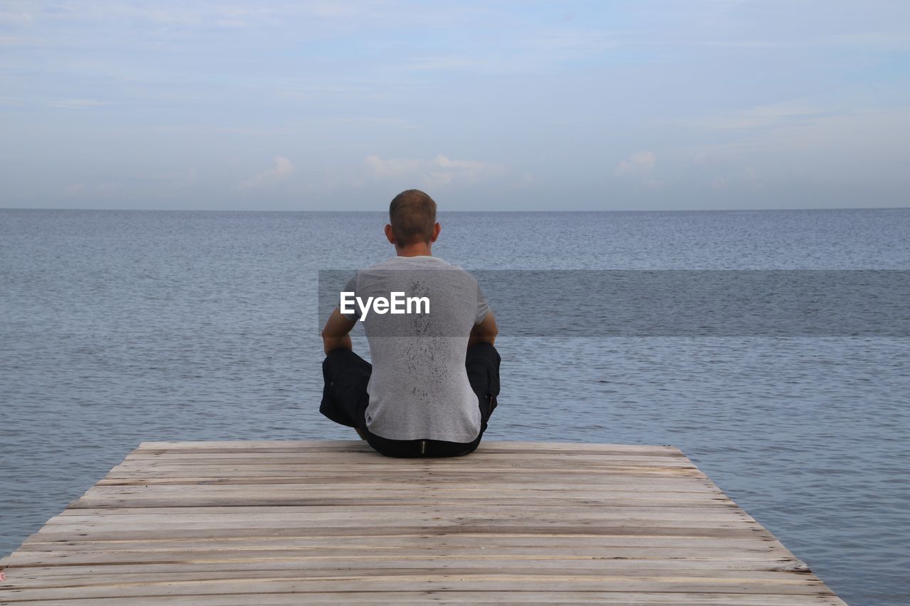 Rear view of man relaxing on jetty in front of the sea