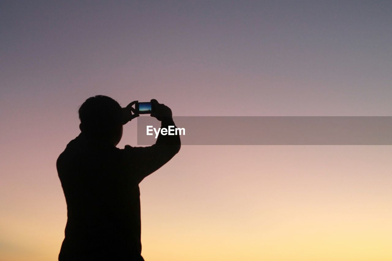 Silhouette man photographing clear sky at dusk