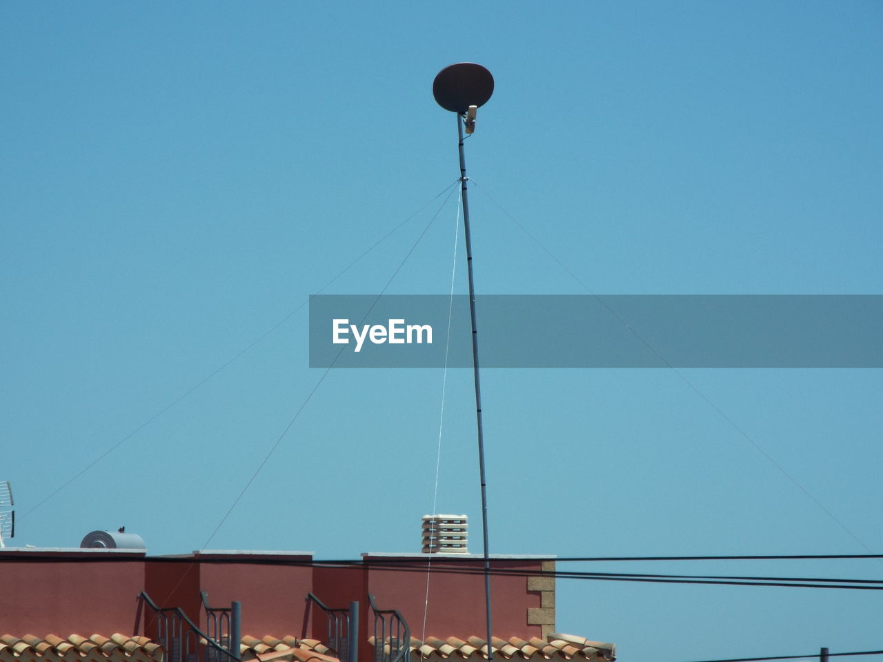 Low angle view of satellite dish and cable over buildings against blue sky