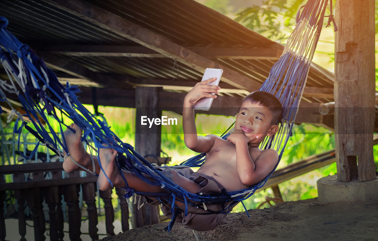 Cute boy lying on hammock taking selfie from smart phone