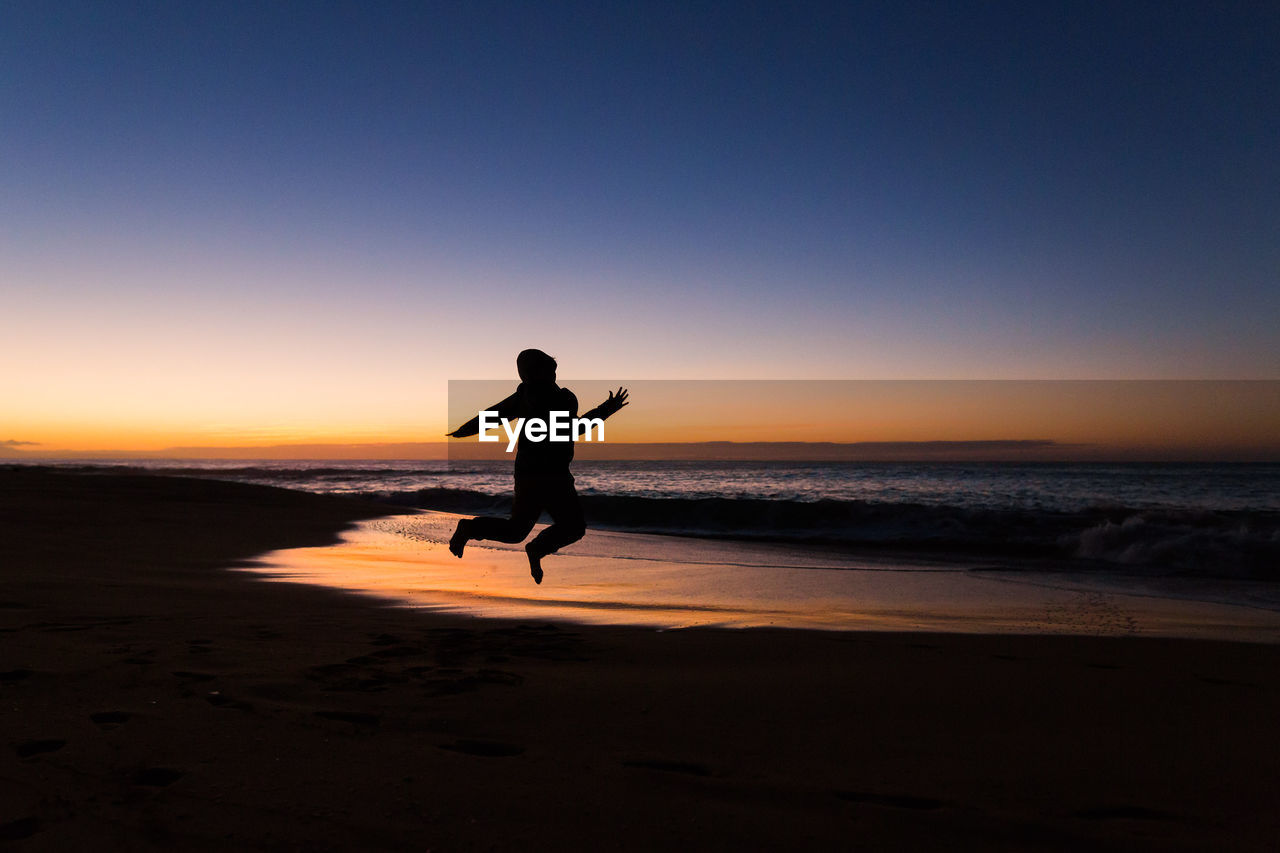 Silhouette boy jumping at beach against sky during sunset