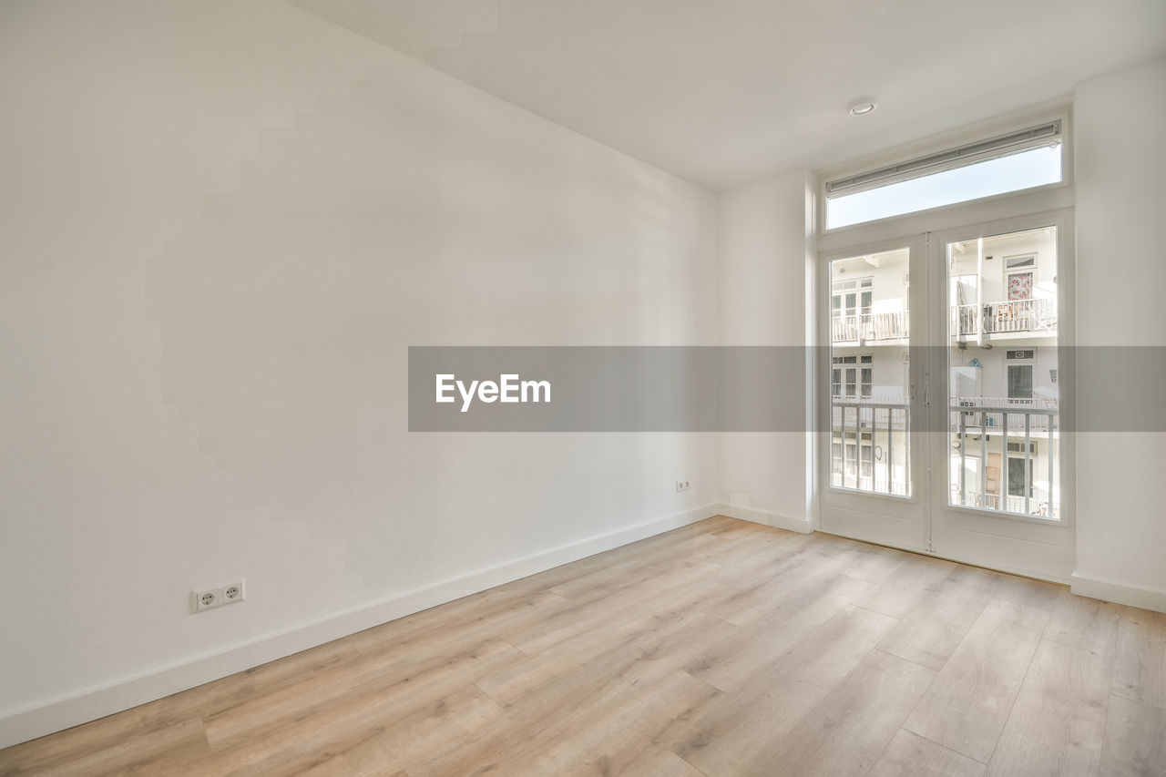 Interior of spacious empty room with white walls laminated floor and open door leading to balcony