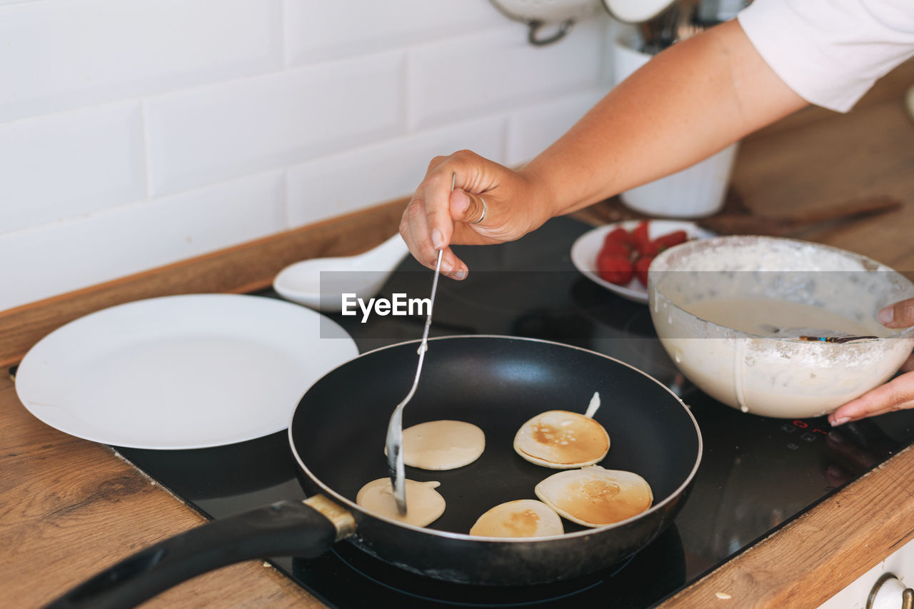 Young woman cooks pancakes in a frying pan in the kitchen at home