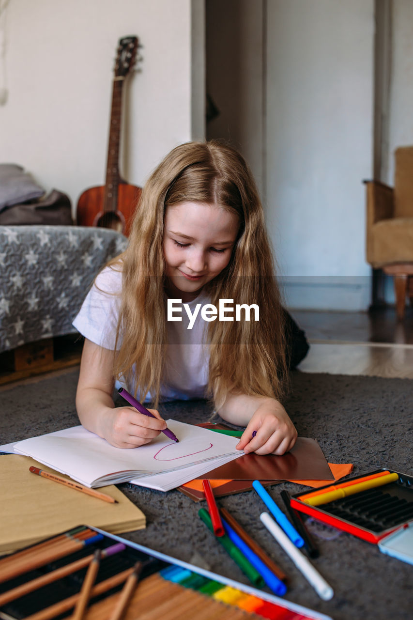 The girl after school plays at home, draws with pencils and felt-tip pens