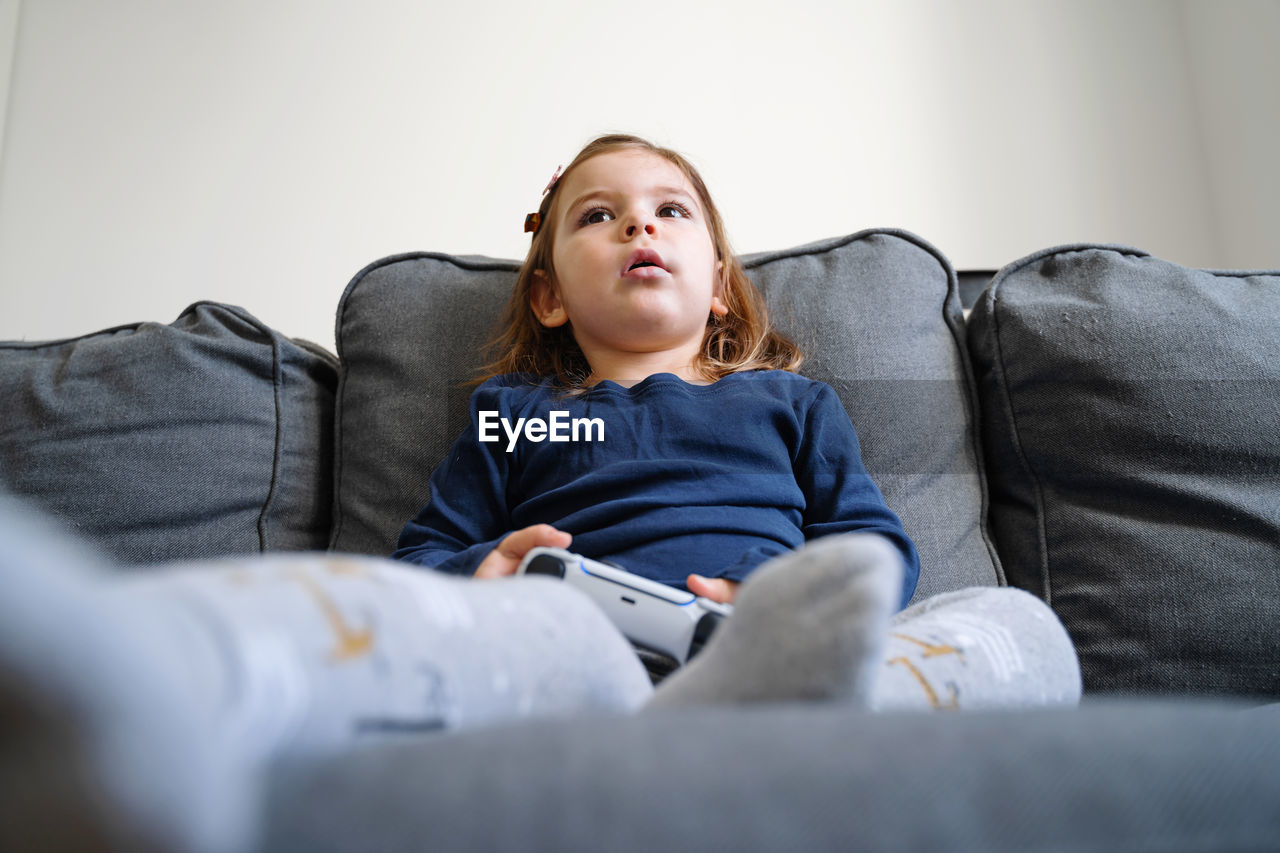 Girl looking away while sitting on sofa at home