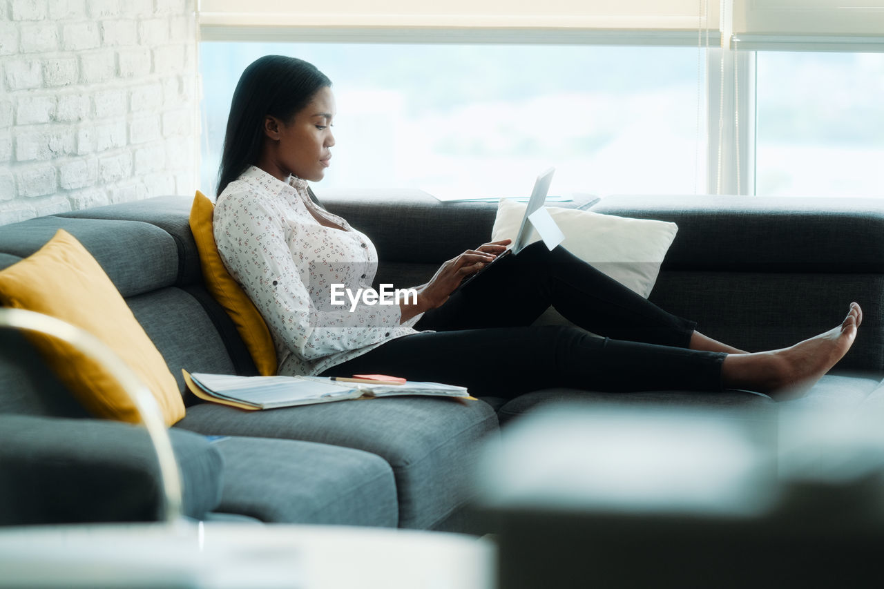 Full length of businesswoman using laptop sitting on sofa at home