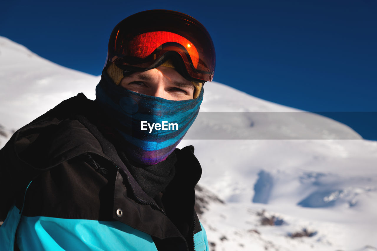 Portrait of a skier in the mountains without a ski mask with a scarf on his face, narrowing his eyes
