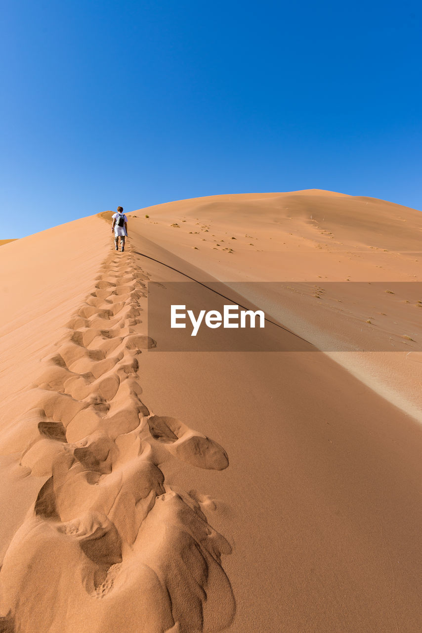 Woman walking on desert against clear sky