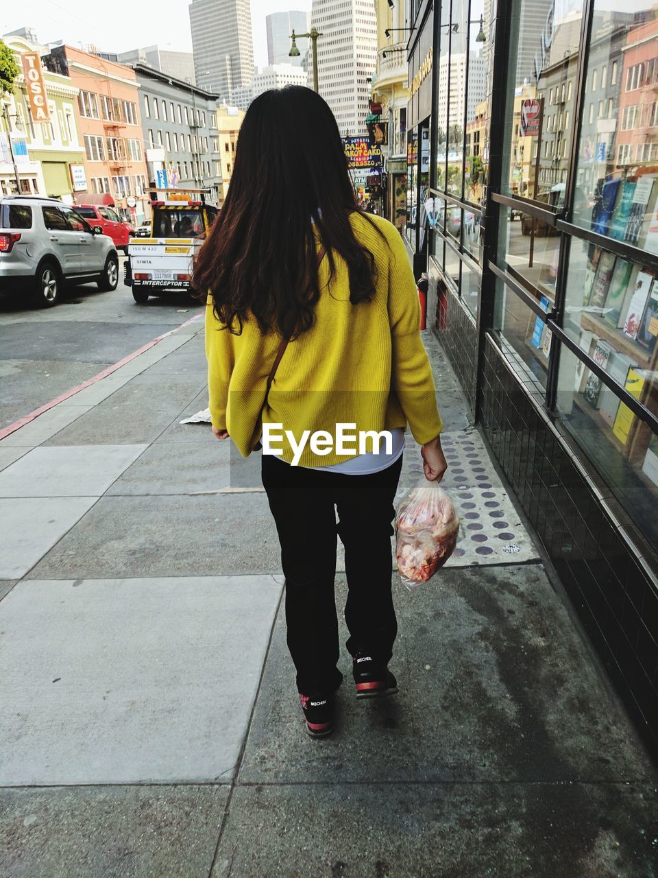 Rear view of woman holding meat while walking on street