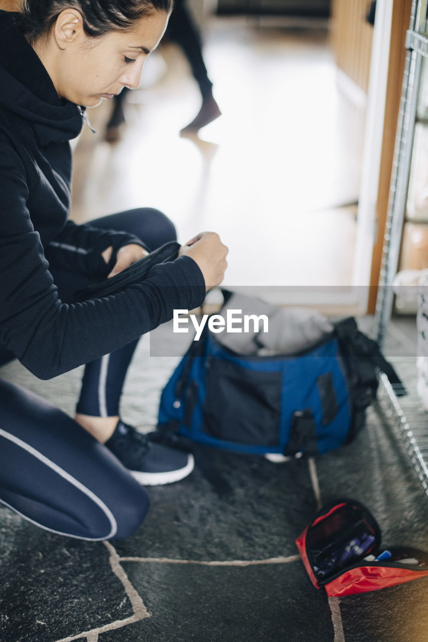 Side view of woman checking diabetes kit while kneeling on floor at home