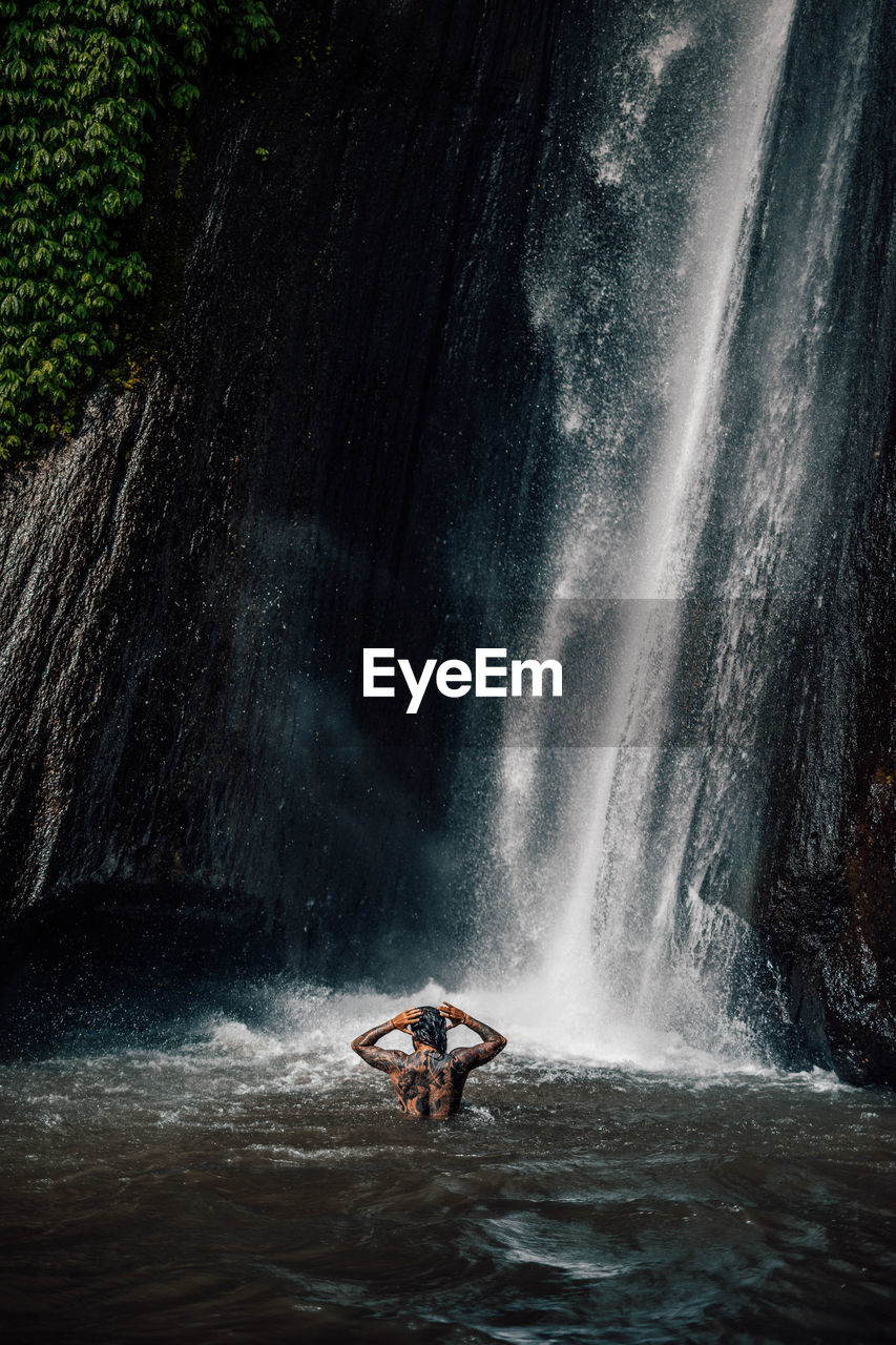 Man swimming by waterfall