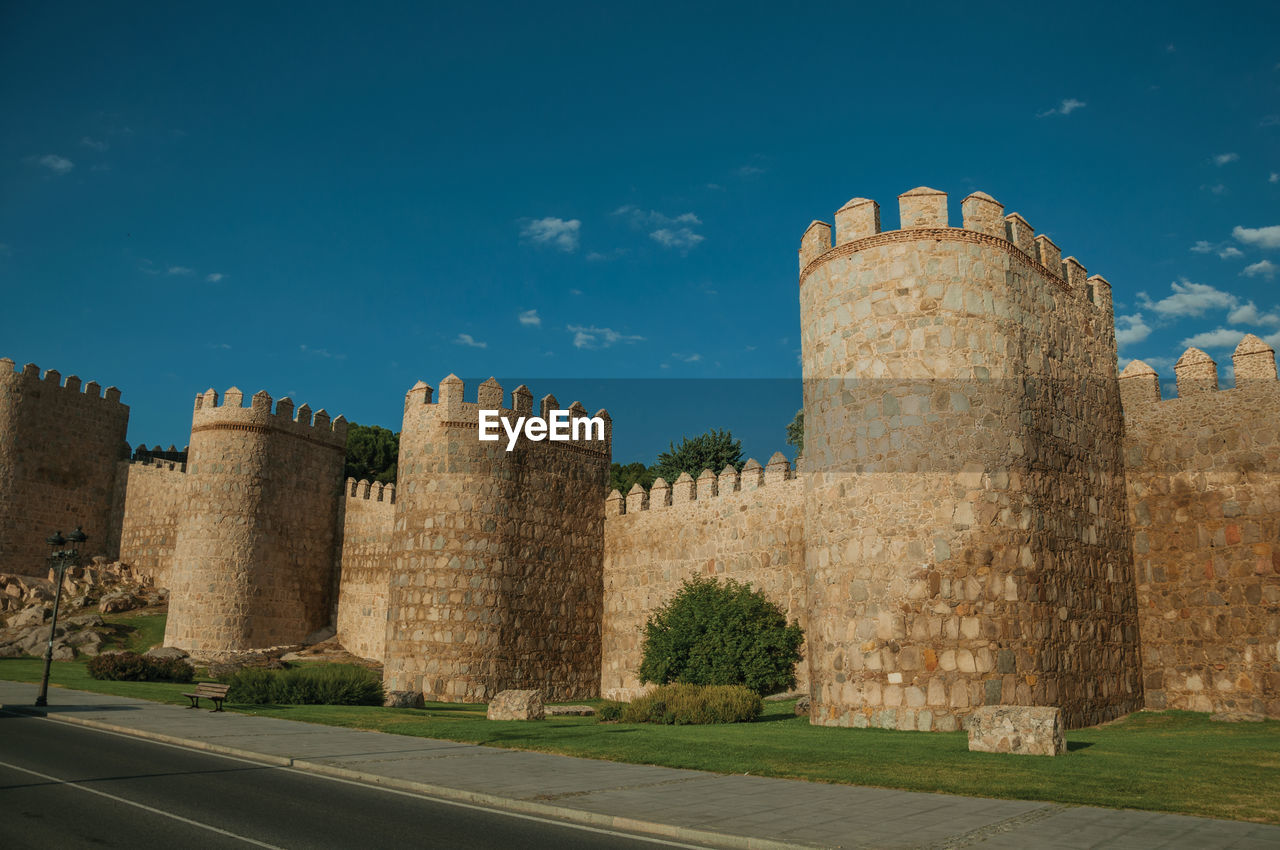 Street and light posts beside stone towers in the large wall encircling the town of avila, in spain.