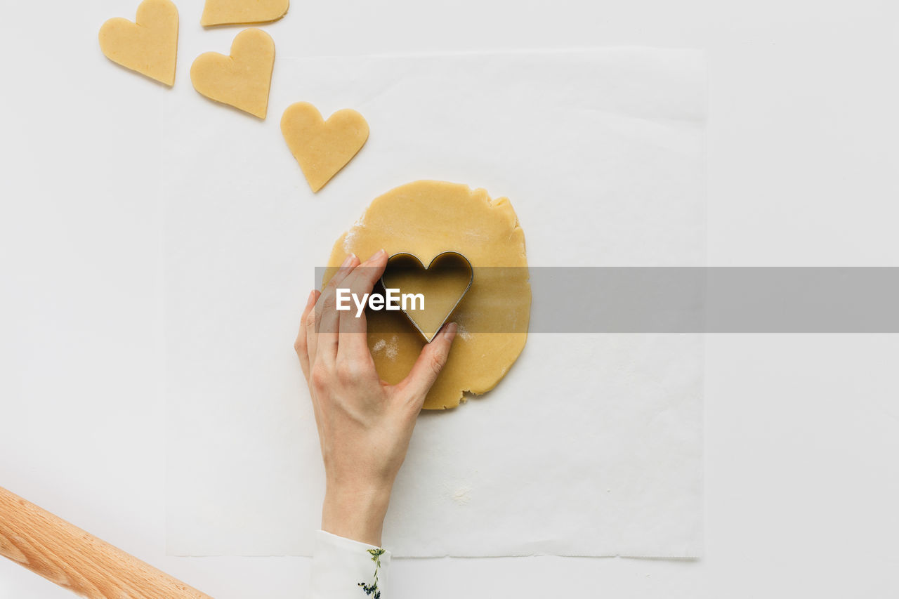 Cropped hand of woman using heart shape cutter on dough