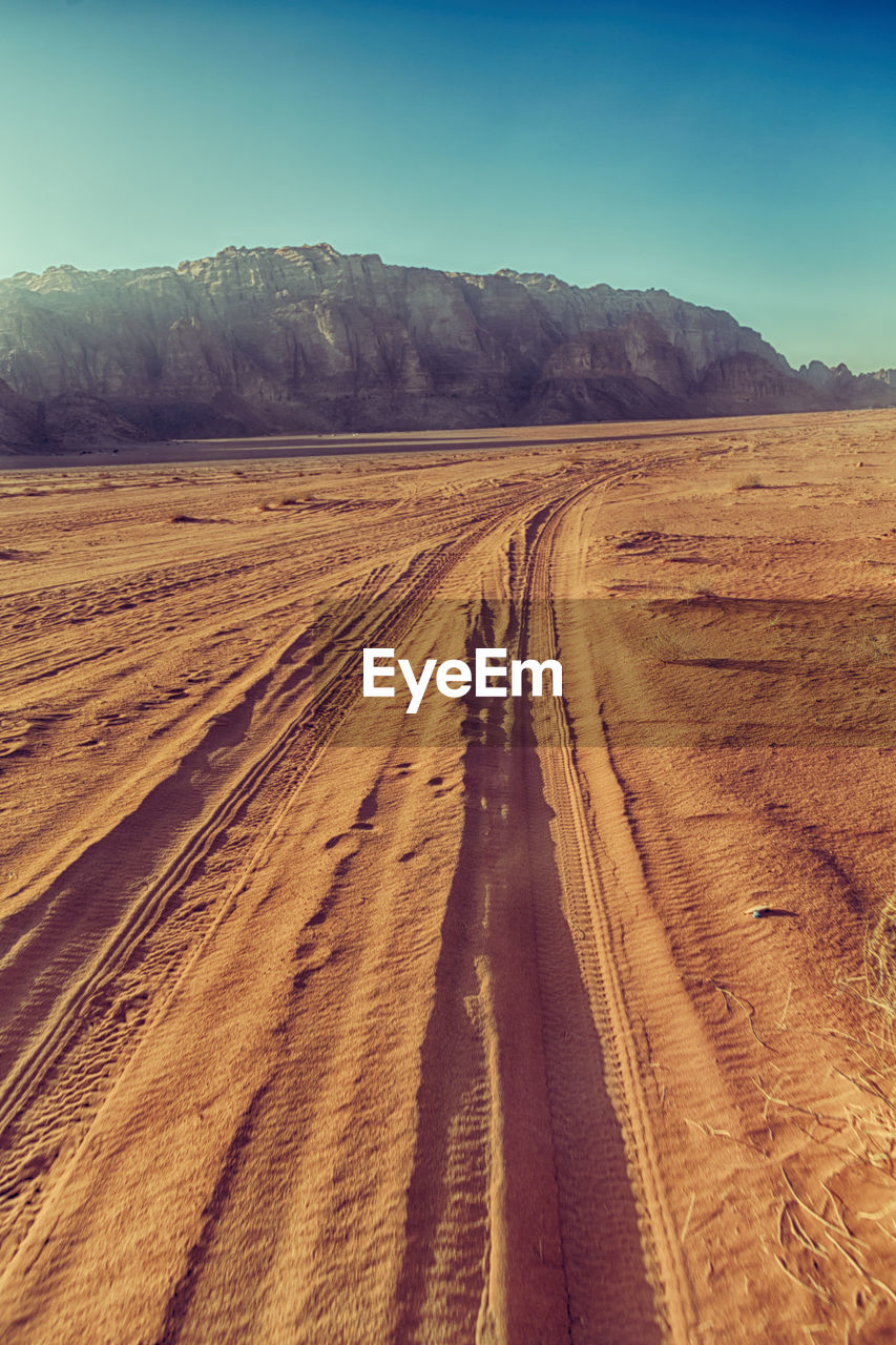 Scenic view of dirt road by land against sky