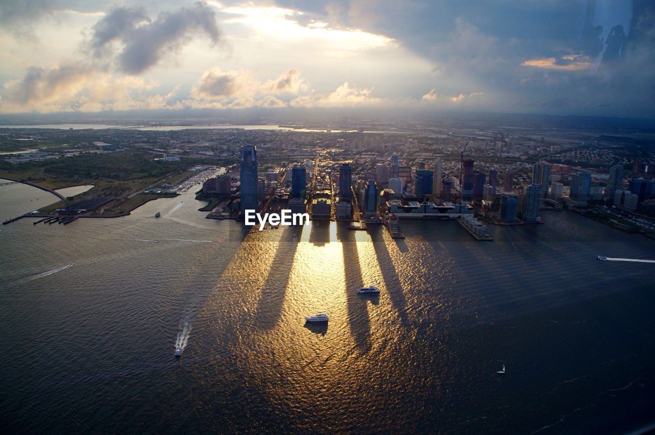 High angle view of cityscape by seashore against cloudy sky