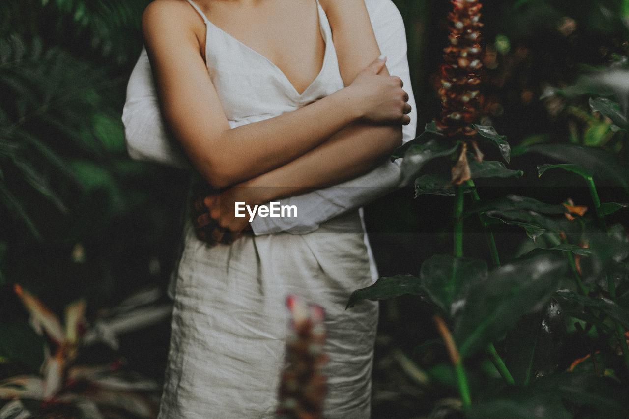 MIDSECTION OF WOMAN HOLDING WHITE STANDING BY PLANTS