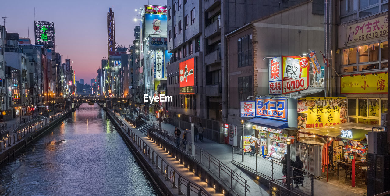 Canal amidst illuminated buildings in city during sunset