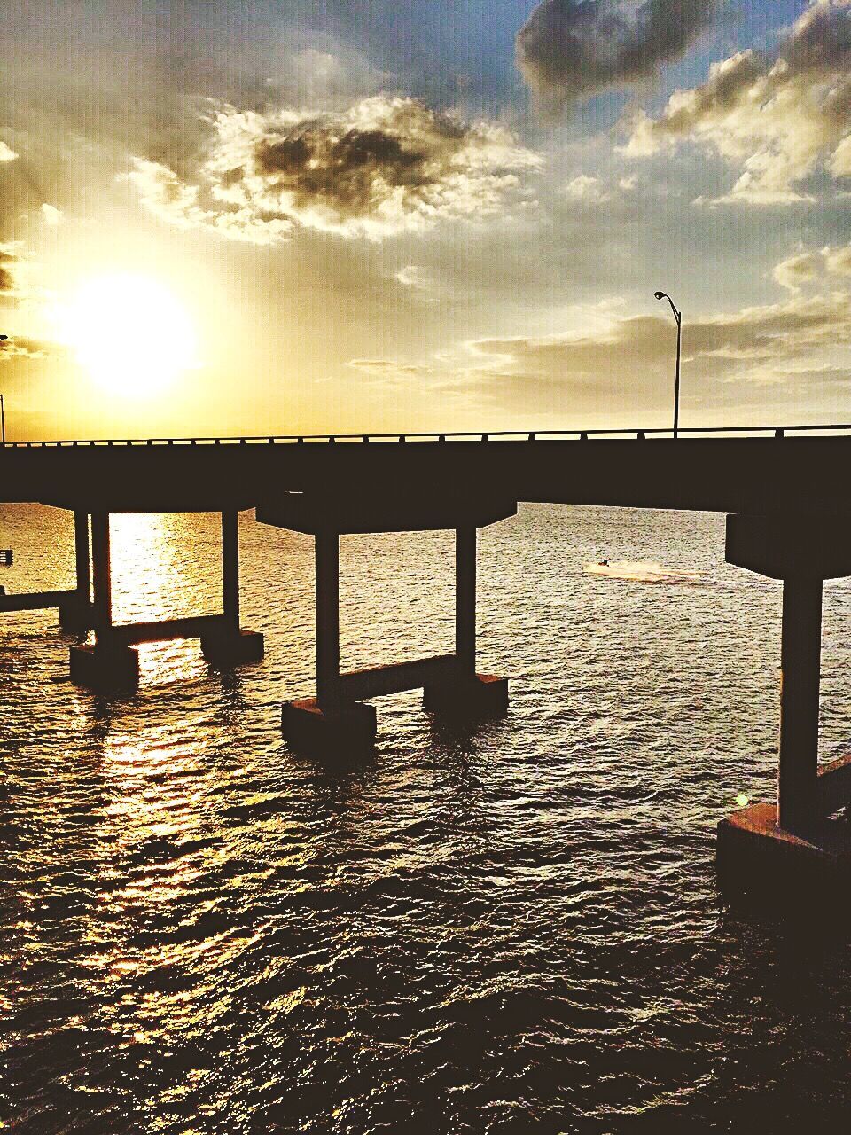 Silhouette bridge over river against cloudy sky during sunset