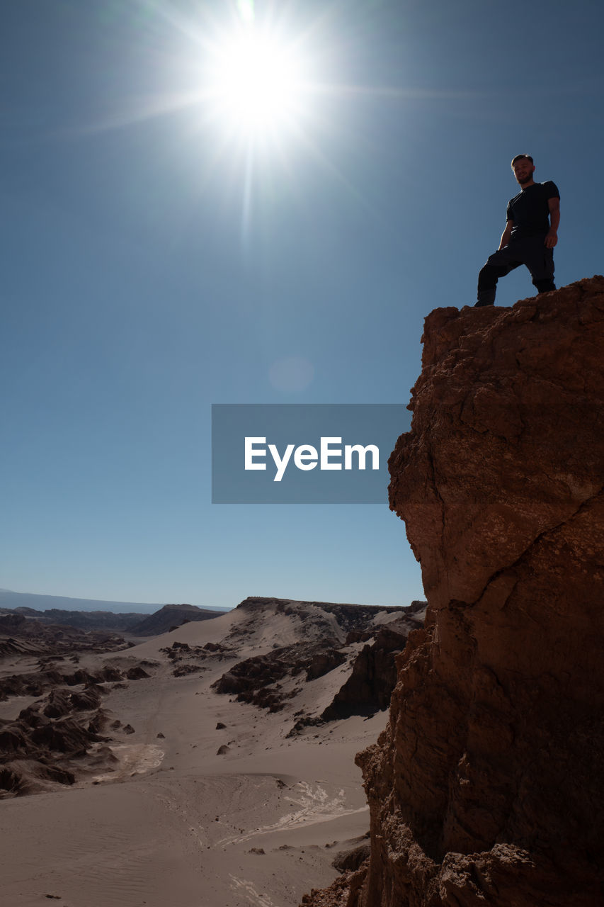 MAN STANDING ON ROCK AGAINST SKY