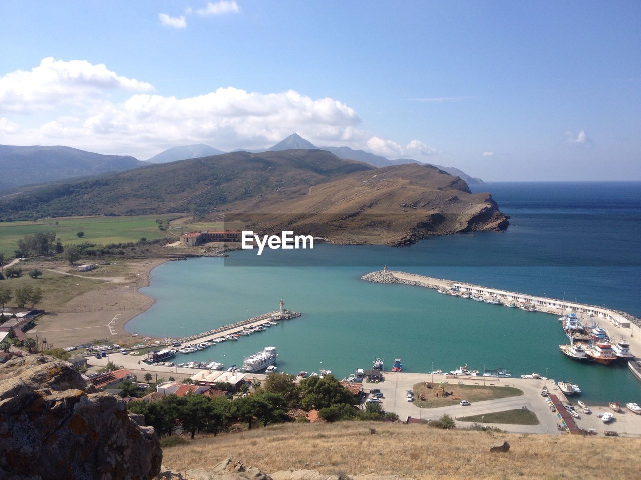 Aerial view of sea and rocky mountains against cloudy sky on sunny day