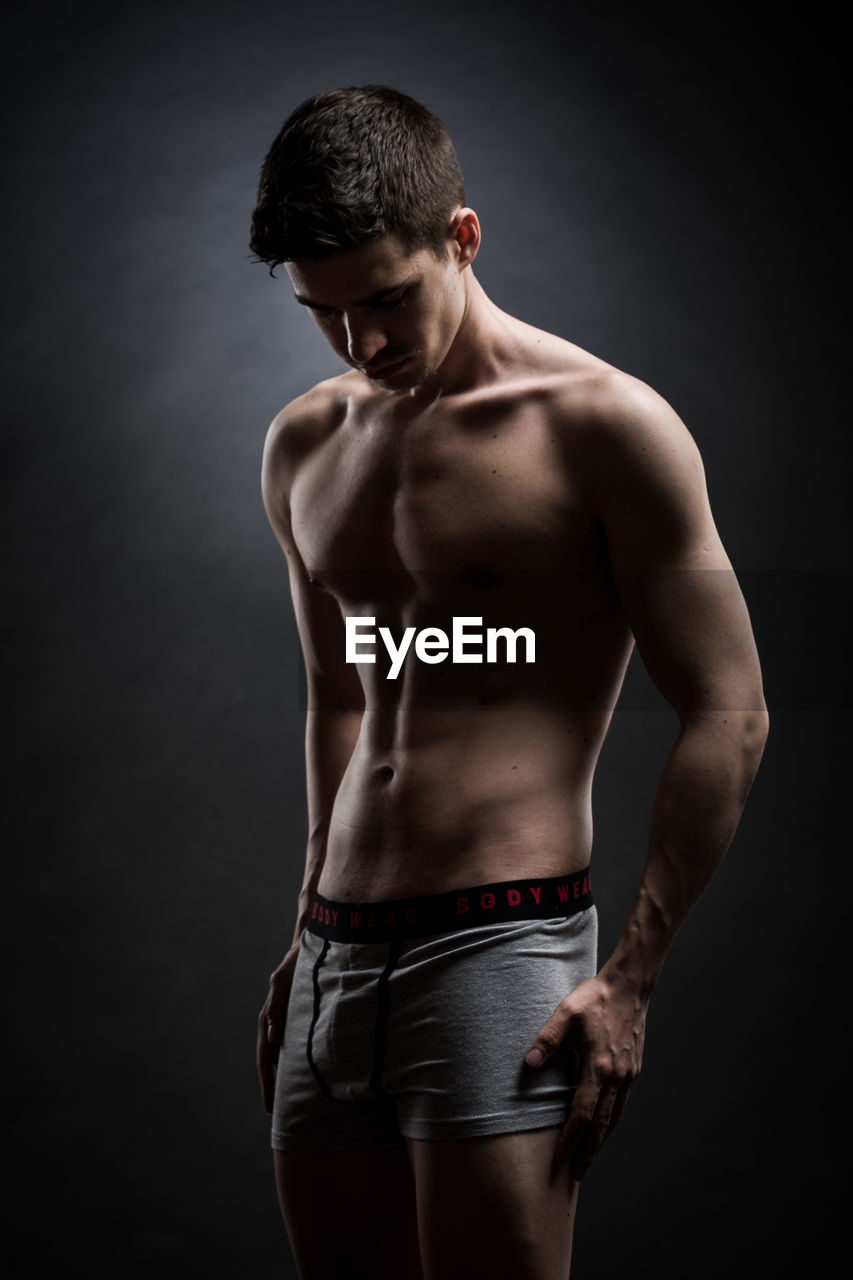 MIDSECTION OF SHIRTLESS MAN STANDING AGAINST BLACK BACKGROUND