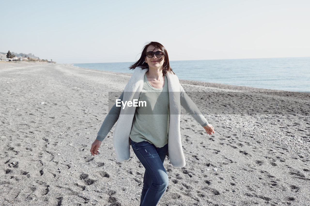 Woman walking on the deserted winter beach, enjoying sunny weather and turning to smile