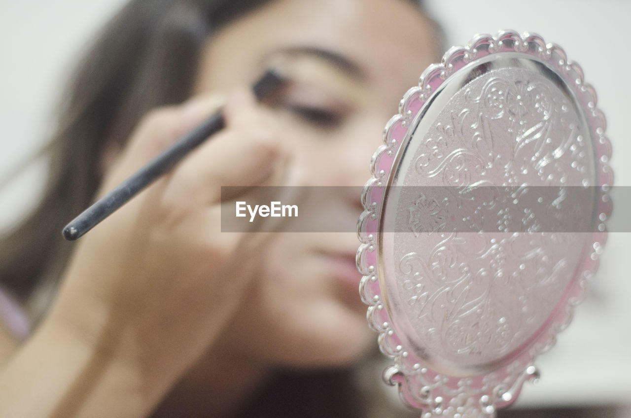 Close-up of woman applying make-up holding hand mirror