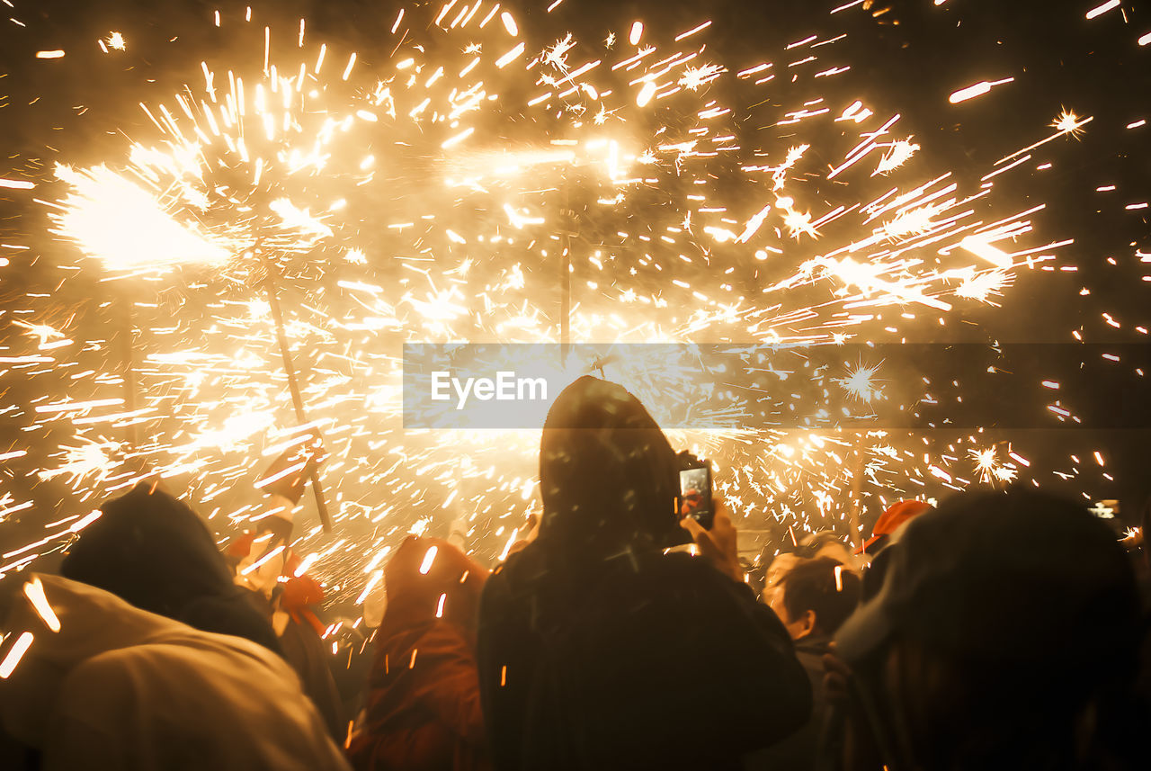 Rear view of people looking at fireworks display against sky at night