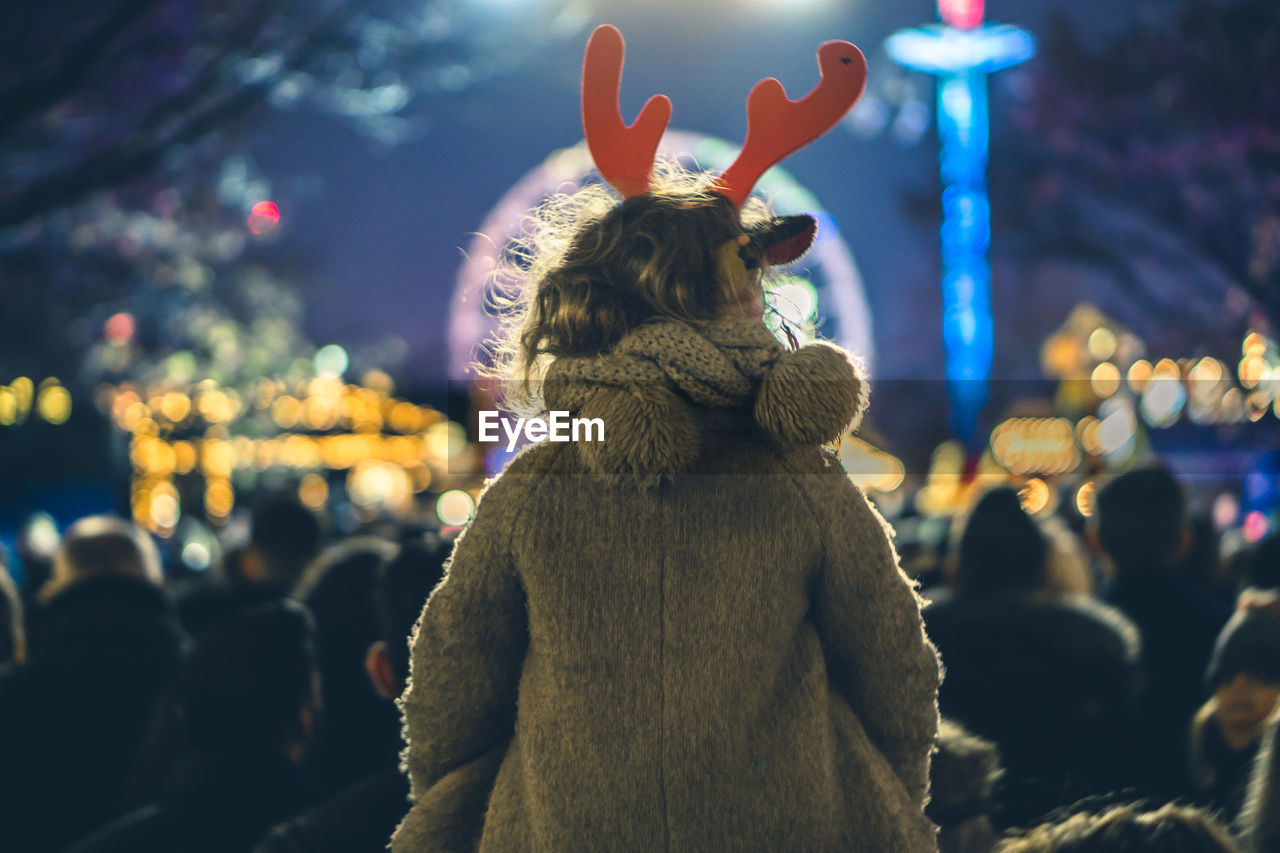 Rear view of girl wearing reindeer headband with crowd in background at hyde park