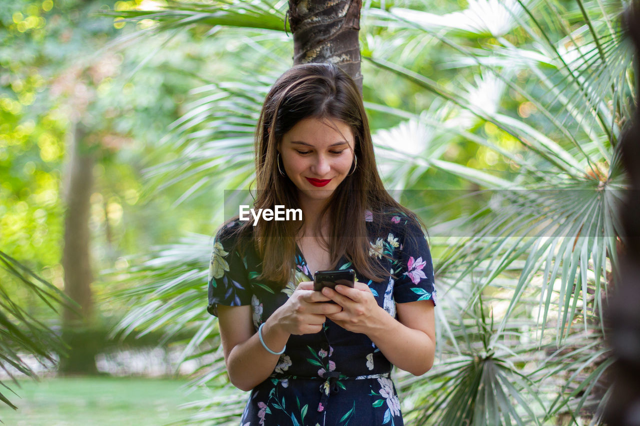 Young woman using mobile phone while standing against trees