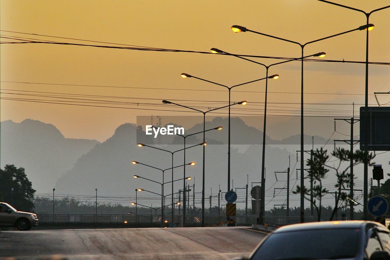 Street lights by road against sky during sunset