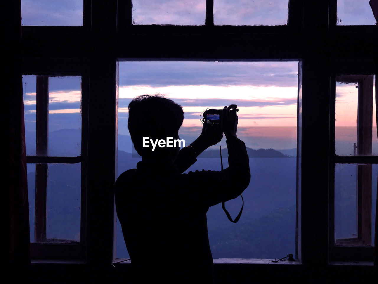 Rear view of silhouette man photographing through window