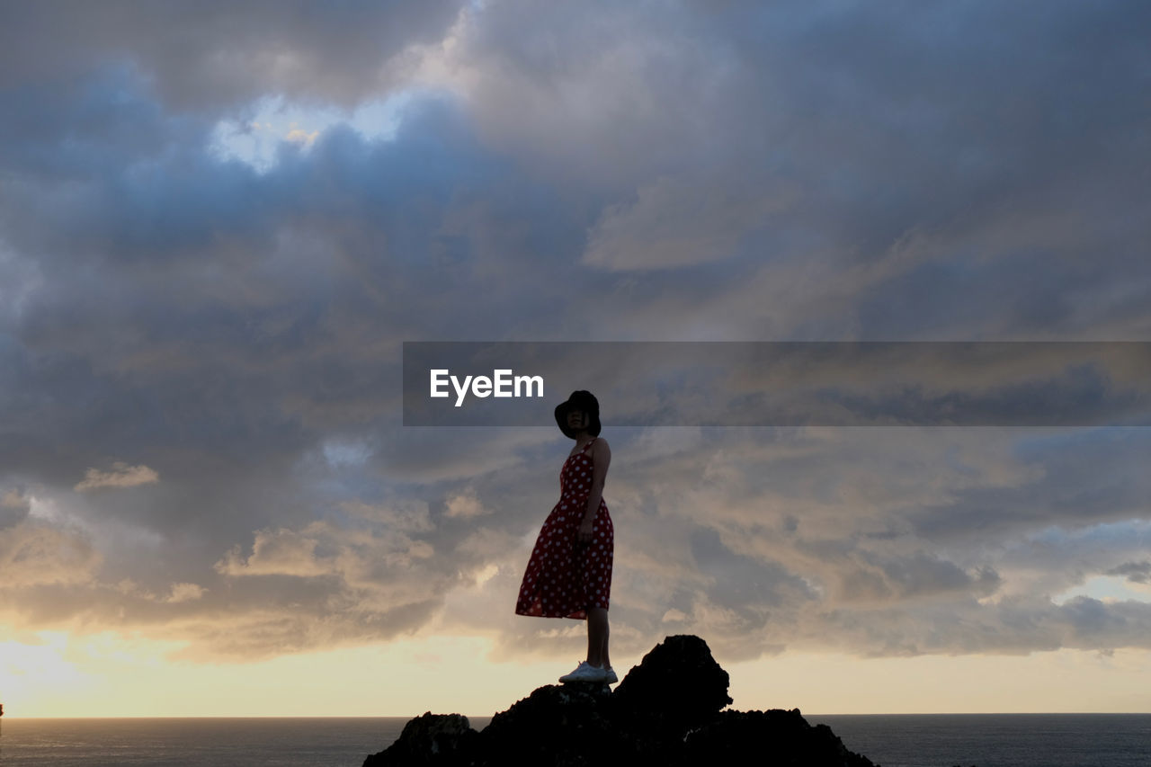 rear view of woman standing on beach against cloudy sky