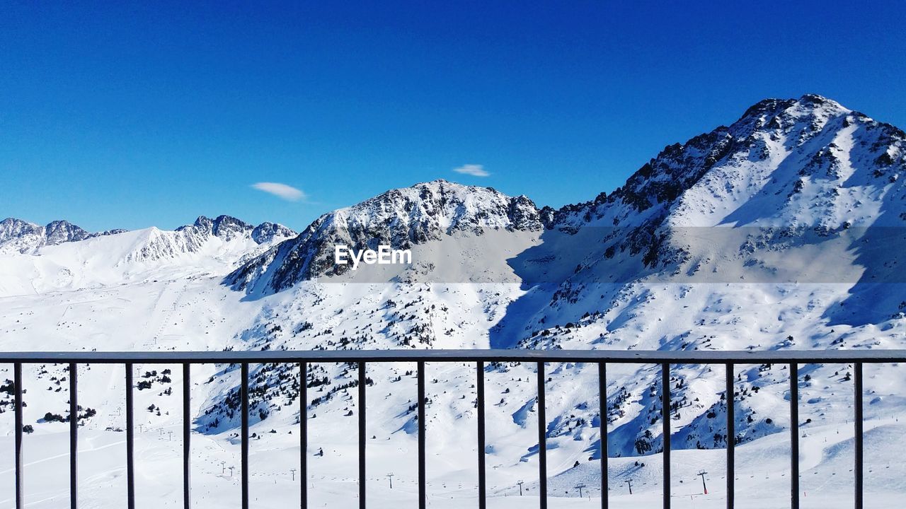Scenic view of snowcapped mountains seen through railing against blue sky