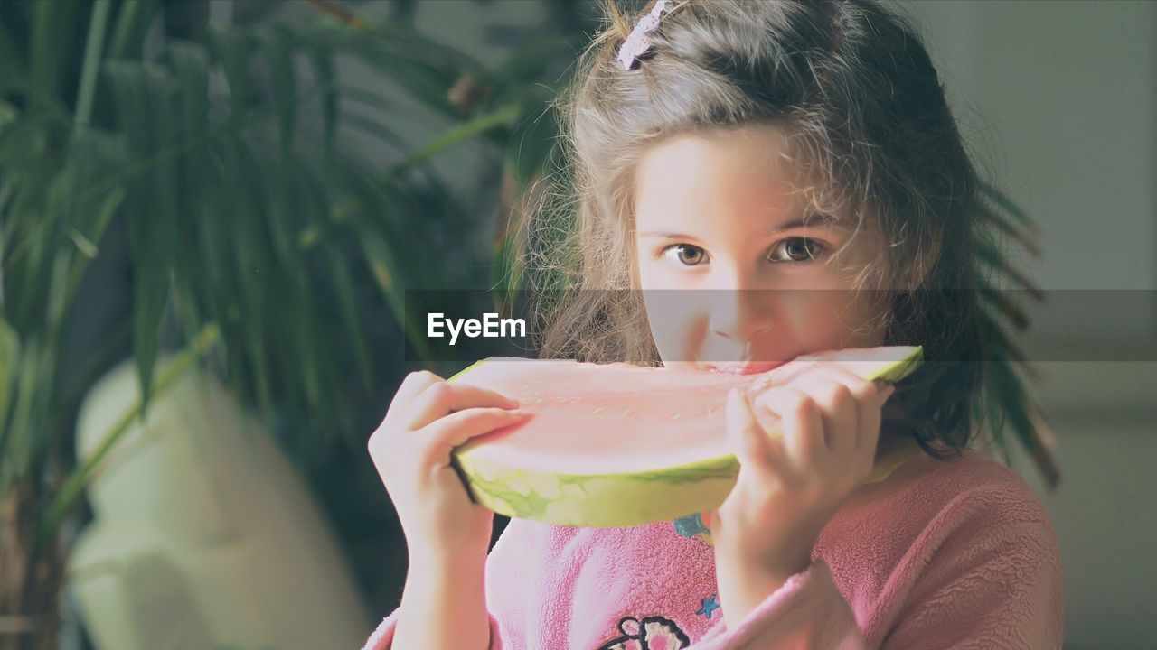 Close-up portrait of girl eating watermelon slice at yard on sunny day