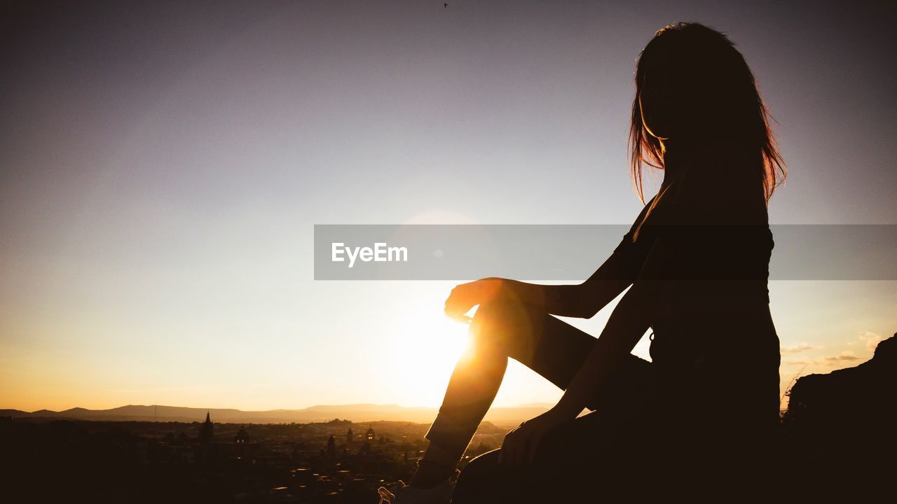 Silhouette of woman sitting against sky during sunset