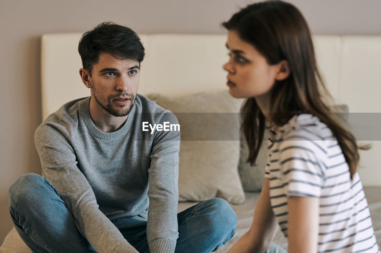 Young man looking at girlfriend while sitting pn bed at home