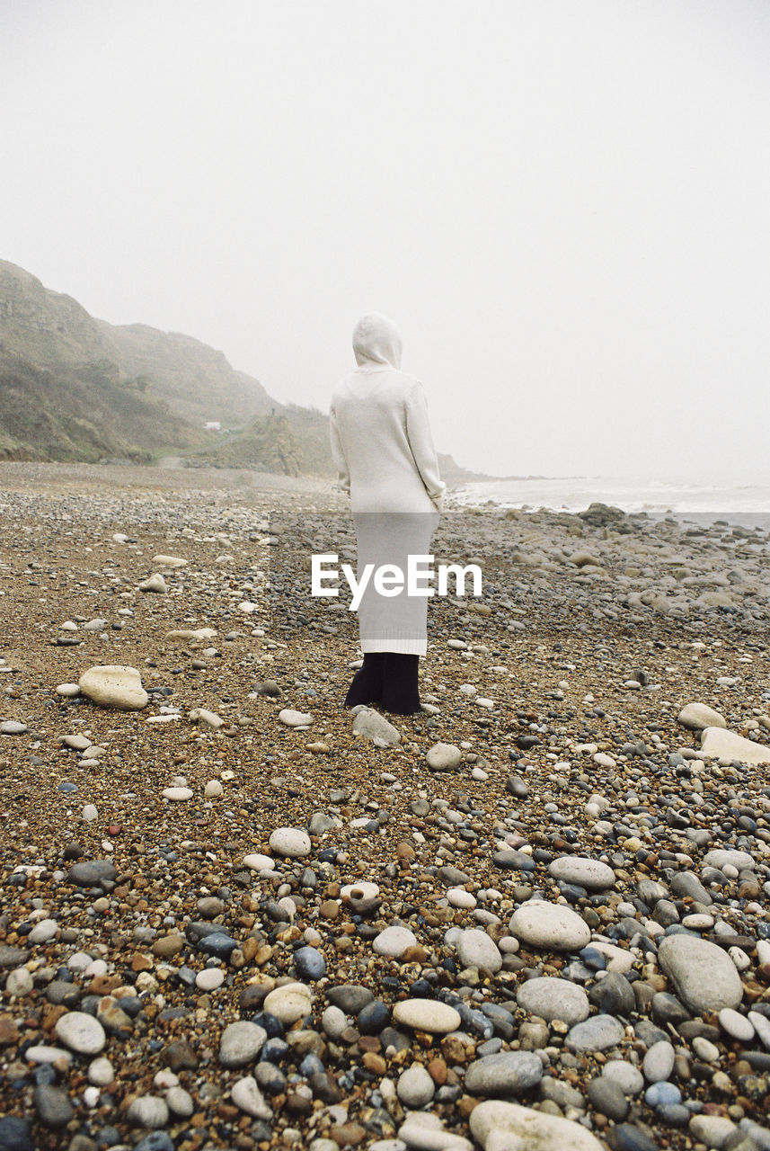 Rear view of woman standing at beach against clear sky