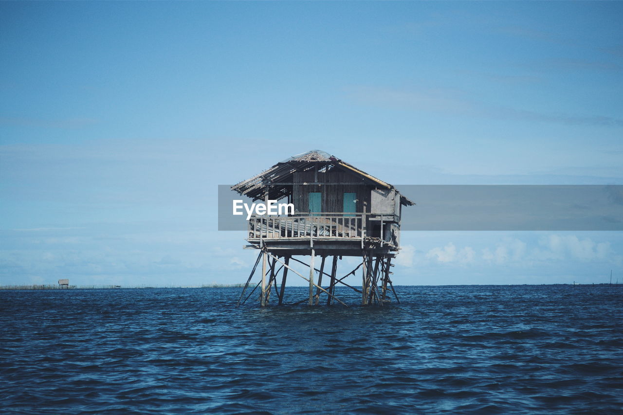 Abandoned stilt house in sea against sky