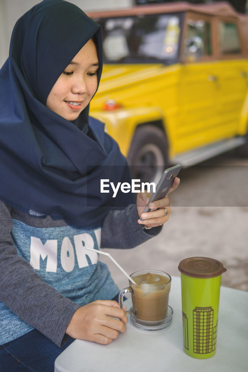 Smiling woman using mobile phone by drink on table