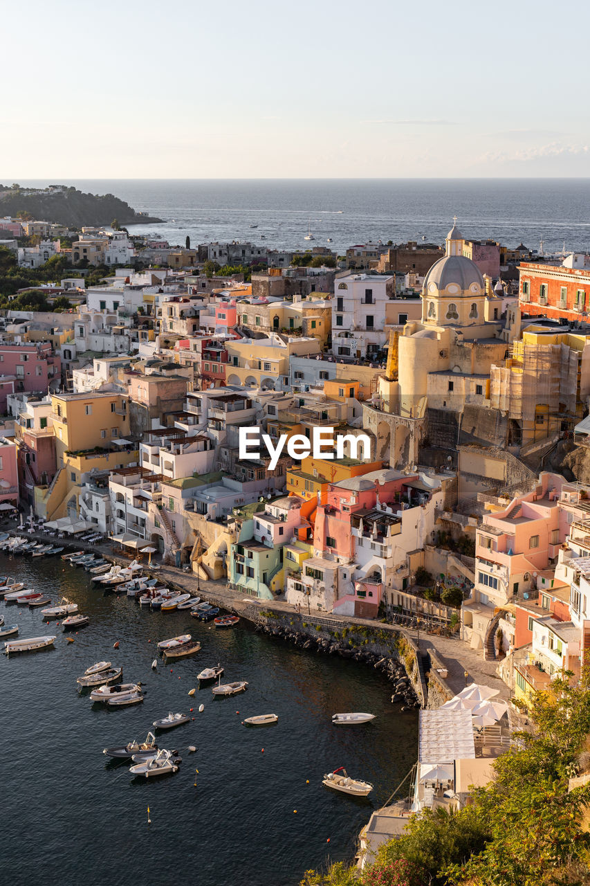 From above of picturesque scenery of costal town with colorful residential buildings located on procida island among sea with moored boats in sunny day