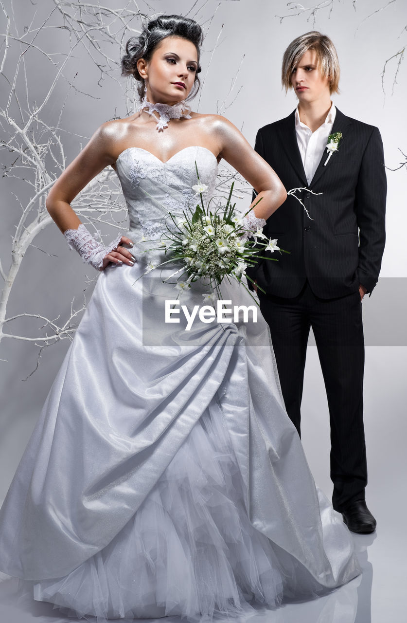 Bride and groom with bare trees standing against white background