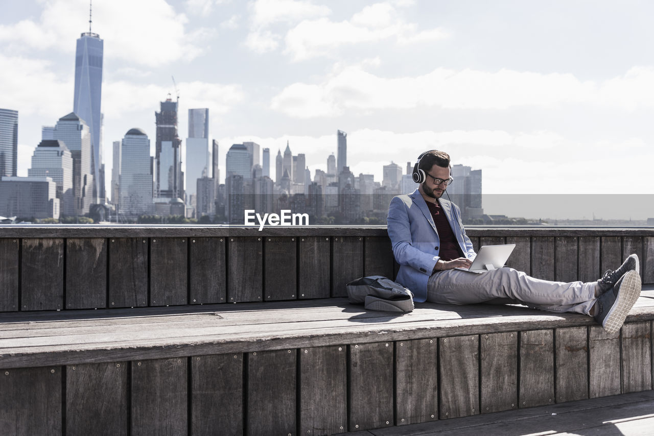 Usa, man wearing headphones using tablet at new jersey waterfront with view to manhattan