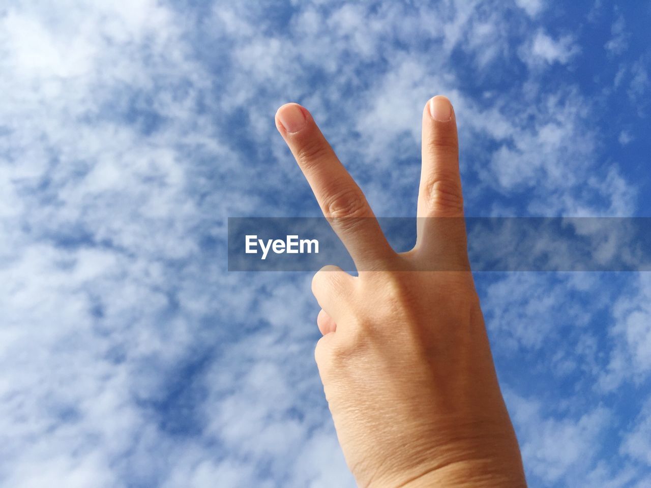 Low angle view of human hand gesturing peace sign against sky