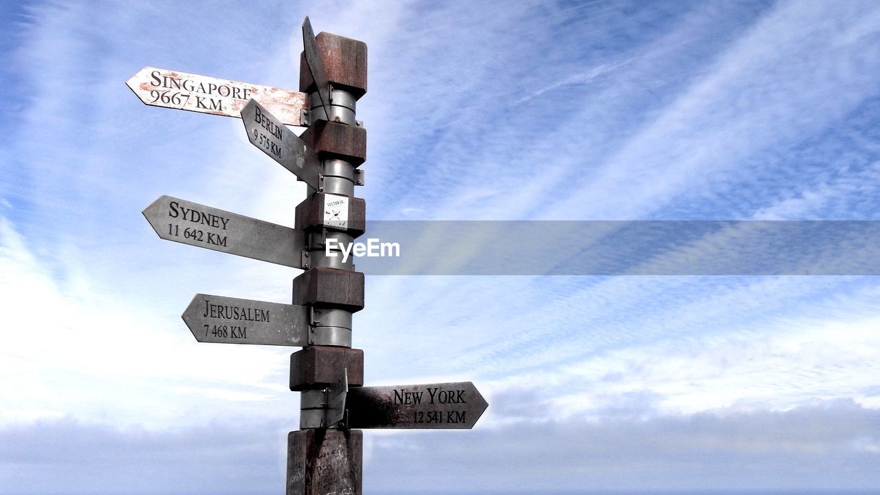 Low angle view of directional sign against cloudy sky