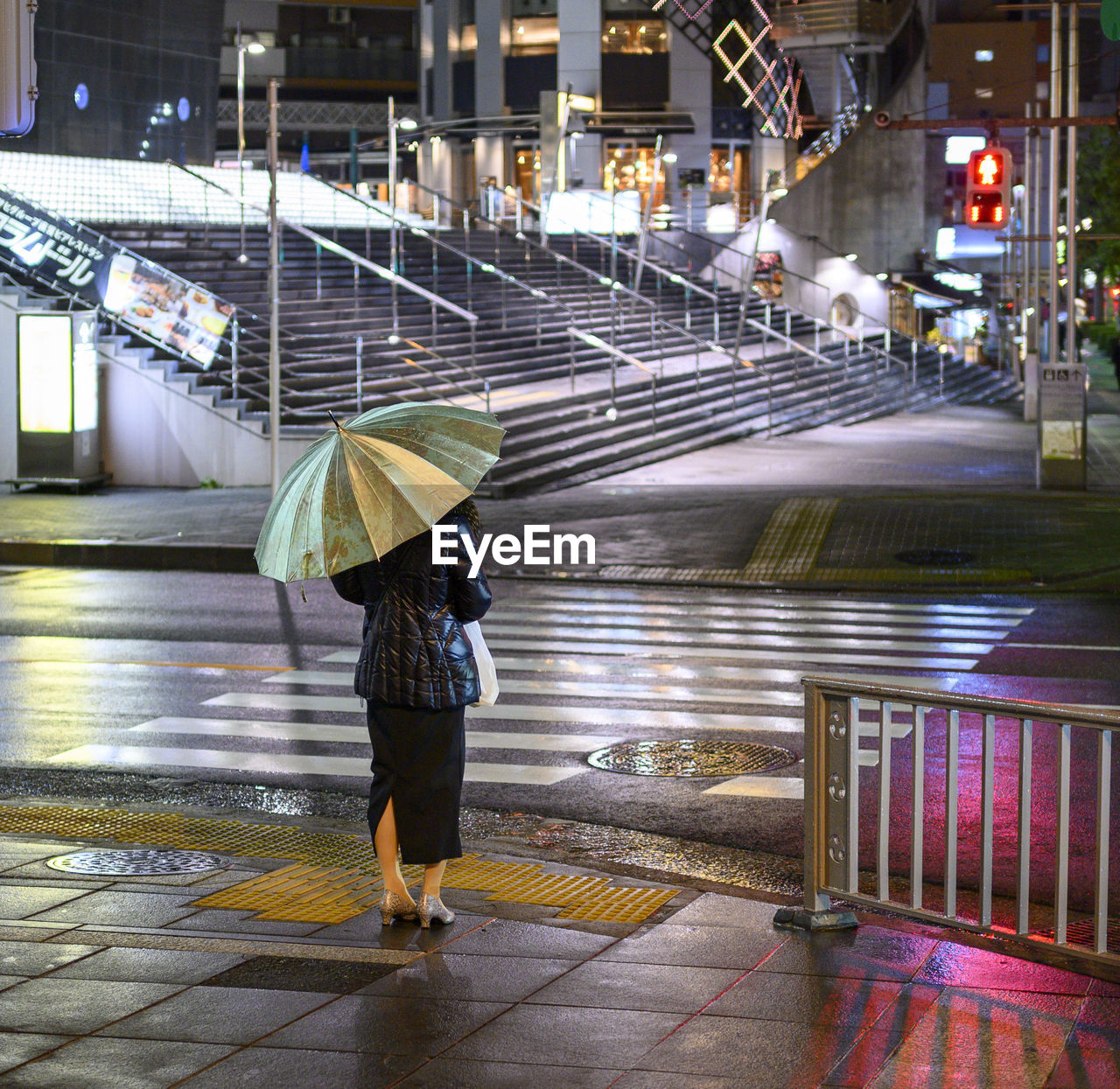 A woman holding an umbrella, waiting to cross the street in tokyo.