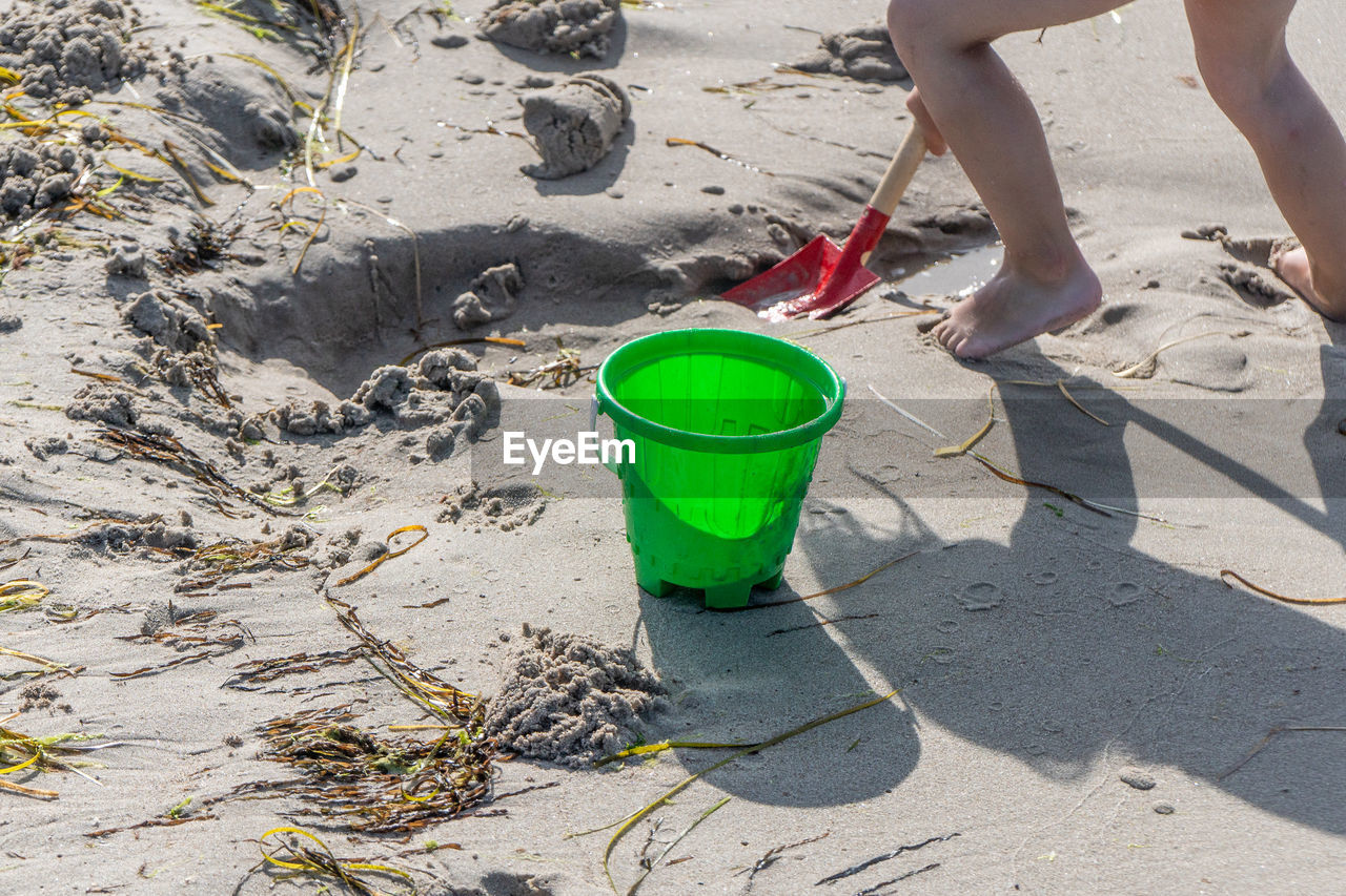 Low section of kid playing on beach with red shovel and green bucket