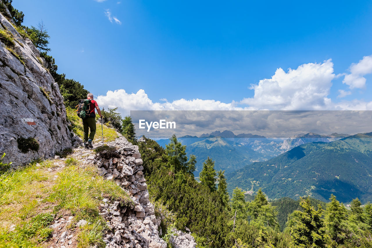 Rear view of man hiking on mountain against blue sky