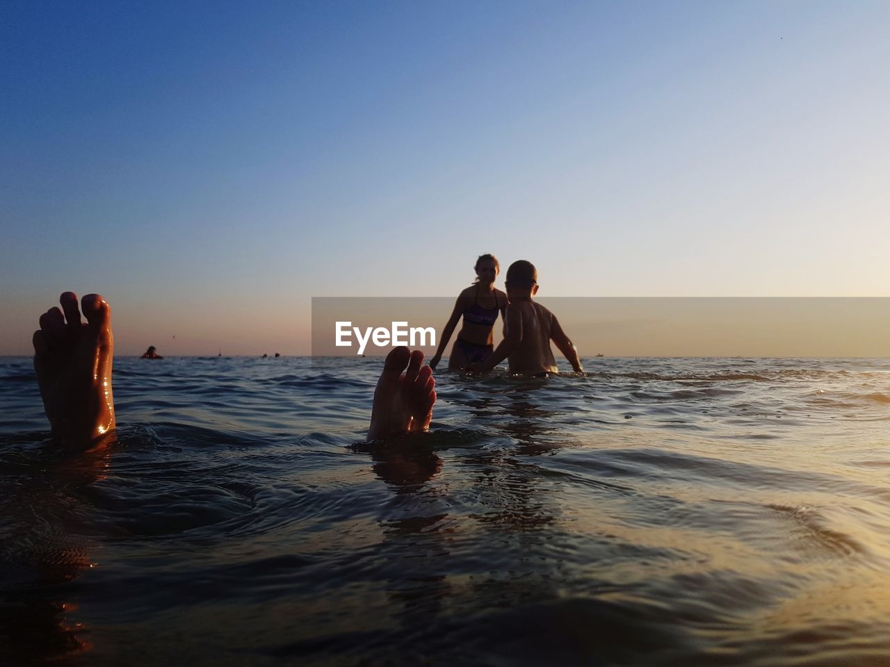 PEOPLE ENJOYING IN SEA AGAINST SUNSET SKY